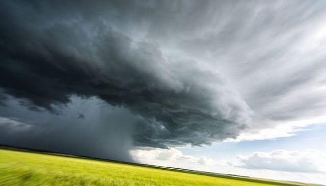 Roaring shelf cloud sweeping across sunlit prairie with heavy rain shaft and dramatic sky