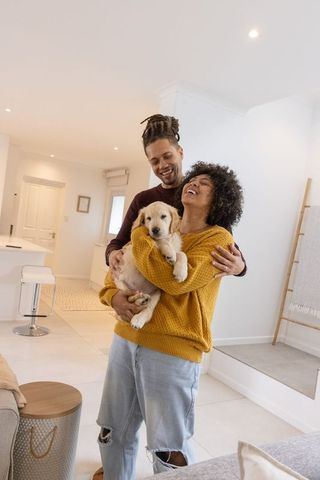 Couple embracing with golden retriever puppy in bright modern home, cozy knitwear