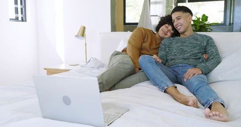 Diverse Couple Relaxing on Bed with Laptop at Home