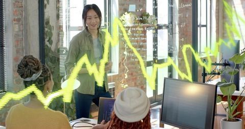 Women developers collaborating and writing code on glass wall in modern loft office
