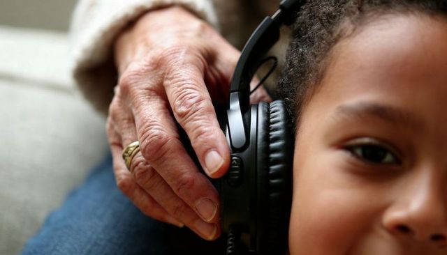 Grandparent adjusting headphones on child's ear, intergenerational bonding closeup