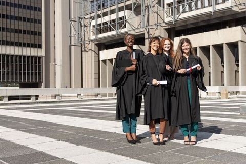 Multicultural women celebrating graduation on urban campus plaza holding diplomas