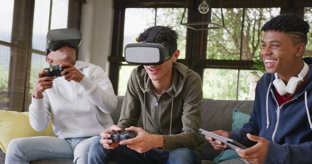 Three teenage boys sitting on a couch in a living room enjoying video games with VR headsets and controllers, having fun and laughing. Great for illustrating youth using technology, modern gaming, social interaction, and leisure activities.