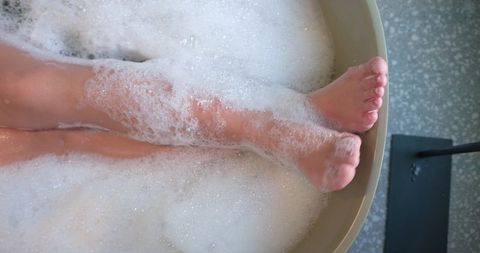 African american woman soaking feet in bubble bath tub for spa pedicure and relaxation