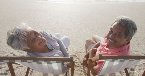 Happy senior couple relaxing on sunbeds at sunset beach