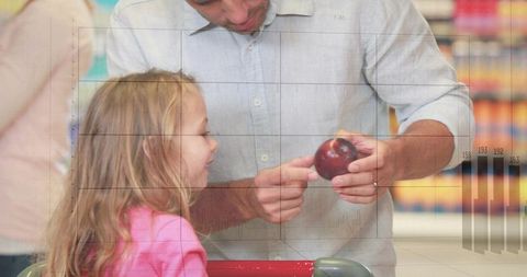 Father offering red apple to daughter in supermarket aisle, joyful family shopping moment