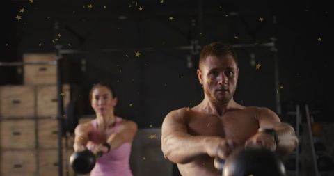Shirtless man and woman swinging kettlebells during intense gym strength training session