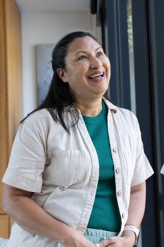Mature woman standing by glass door smiling, wearing button shirt, green top and smartwatch