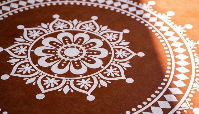 Hand-painting white mandala on rustic brown tabletop with sunlit shadow