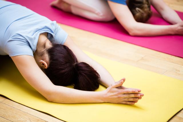 Group of individuals performing child's pose yoga exercise on colorful mats in a fitness studio. Ideal for use in articles or advertisements related to yoga, fitness, wellness, group exercise classes, and healthy living.