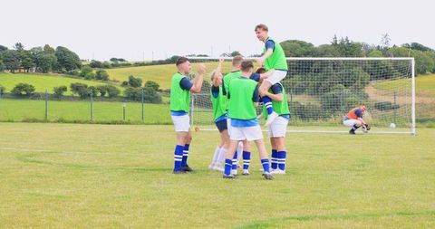 Soccer team celebrating victory outdoors with joyful lifting