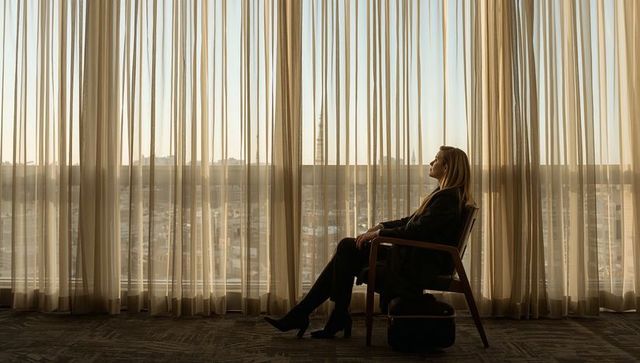 Businesswoman sitting by hotel window gazing at city skyline in soft morning light