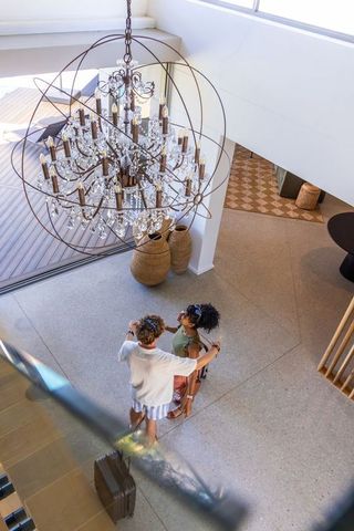 Young couple standing under crystal chandelier in double-height modern foyer with luggage