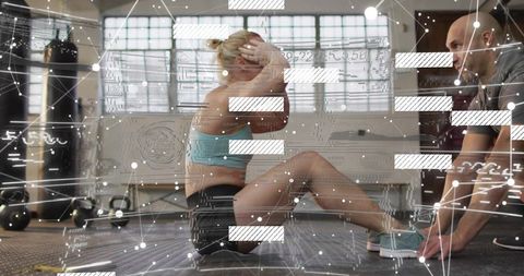 Female trainee doing sit-ups while trainer holding feet in gym with digital overlay