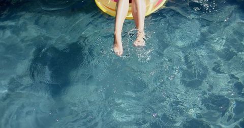 Teenage girl relaxing legs in pool from yellow float