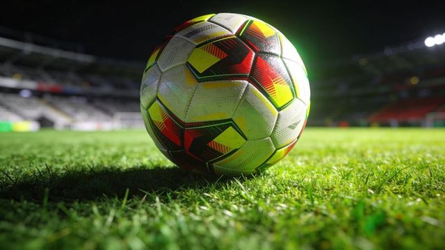 Resting multicolor soccer ball reflecting floodlights on night stadium pitch