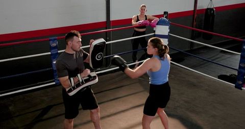 Boxing coach training fighter with focus pads in ring during punching drills
