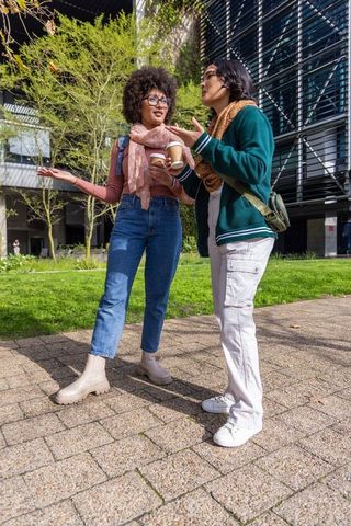 Multicultural young women standing and talking on campus holding coffee cups on sunny walkway