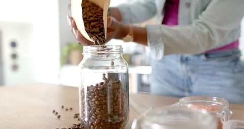 Woman Pouring Fresh Coffee Beans Into Glass Storage Jar