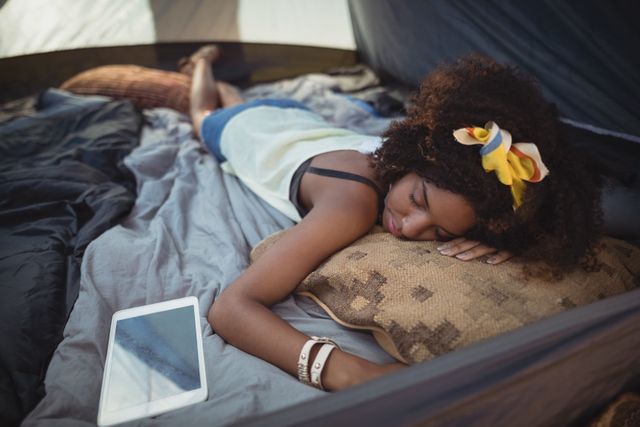 High angle view of young woman sleeping by tablet in tent