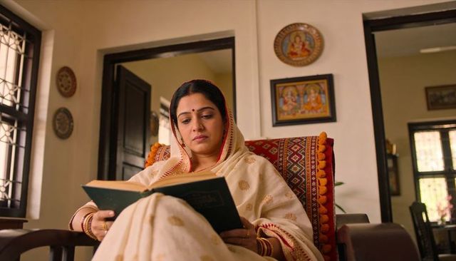 Serene indian woman reading in cream saree with red border on ornate living room chair