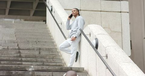 Young man leaning on curved stone balustrade talking on smartphone in urban staircase