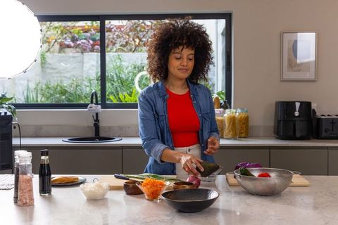 African American woman preparing avocado meal on modern marble kitchen island in home