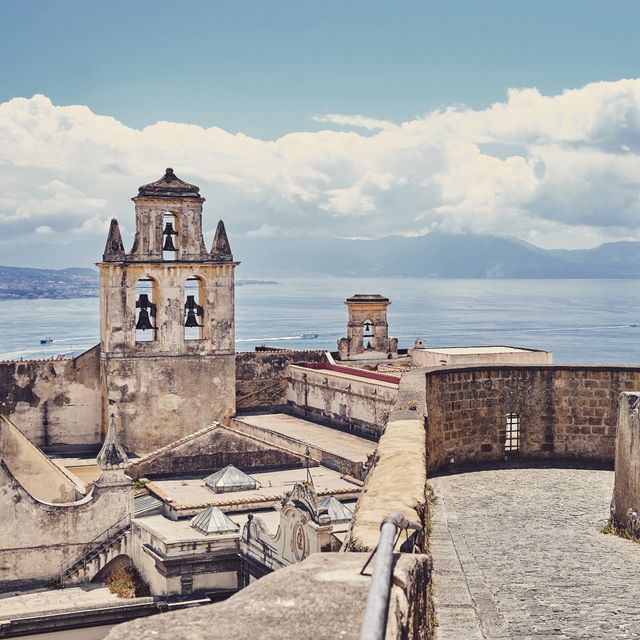 Historic fortress with stone walls and towers stands majestically overlooking a tranquil sea. The background features a beautiful blue sky with scattered clouds. Ideal for travel blogs, heritage site promotions, tourism campaigns, and history-themed content.
