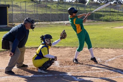 Batter swinging at home plate with catcher and umpire during sunny baseball game