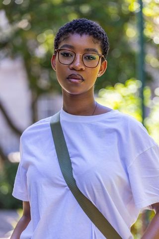 Young woman wearing glasses and white tee outdoors with green crossbody strap