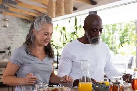 Mature couple enjoying sunny kitchen breakfast pouring orange juice and sharing fruit