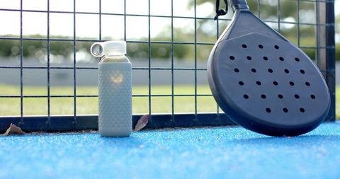 Padel court hydration: pale blue reusable bottle standing beside black padel racket