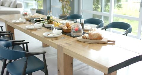 Minimalist light-wood dining table featuring crusty bread, wine and glassware in sunlit room