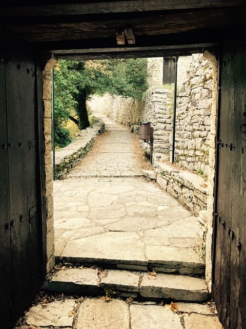Cobblestone path seen through aged castle gate with stone walls on both sides. Ancient medieval architecture invites exploration and evokes historical ambiance. Ideal for themes related to tourism, history, heritage, and nature trails.
