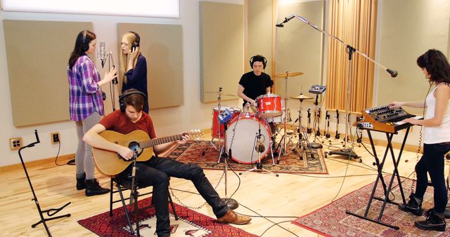 Young band recording music in professional sound studio with various instruments including guitar, drums, keyboard, and microphones. Suitable for use in topics related to music production, band practice, teamwork in creative industries, and professional audio recording environments.