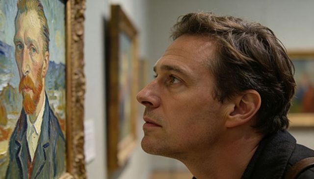 Man leaning close studying oil portrait in museum gallery, contemplating brushwork