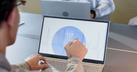 Coworkers collaborating over laptop showing ecg dashboard and heart rate data at meeting