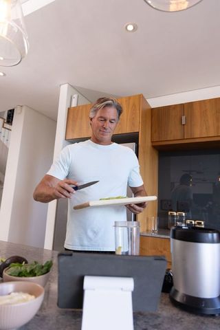 Middle-aged man chopping avocado at modern kitchen island while following tablet recipe