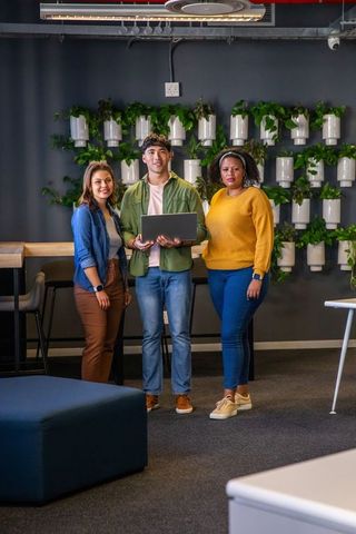 Diverse team collaborating in modern office lounge with laptop and living wall plants