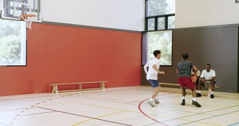 Multicultural friends practicing basketball crossovers and drives on indoor court