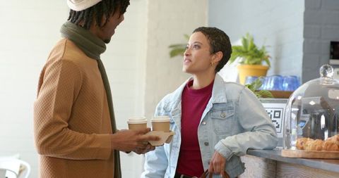 Diverse customers sharing conversation at cafe counter with takeaway coffee and croissants