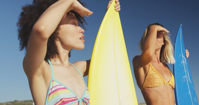 Diverse women in bikini holding surfboards and talking on the beach. Summer, free time, friendship, vacation.