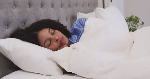 African american woman sleeping peacefully in white bedding wearing blue satin pajamas