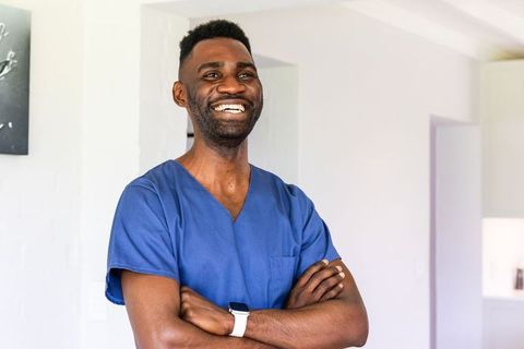 African american healthcare professional smiling in home wearing blue scrubs and smartwatch