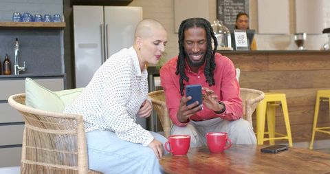 Diverse couple sharing smartphone while enjoying coffee in cozy cafe