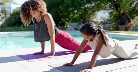 Mother and Daughter Practicing Yoga by the Pool on Sunny Day
