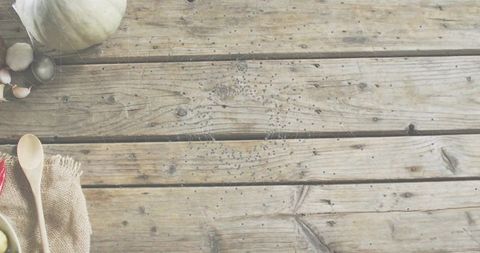 Rustic wooden tabletop showcasing spoons, garlic, olives and gourd with copy space