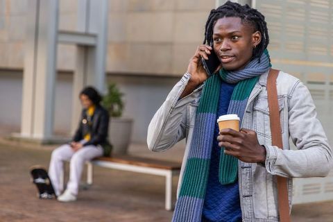 African american man talking on smartphone while holding takeaway coffee in urban plaza