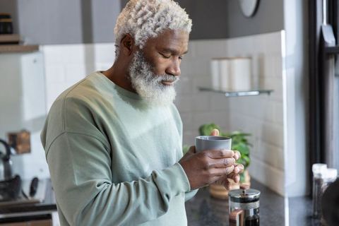 Senior african american man savoring morning coffee with french press in sunlit kitchen