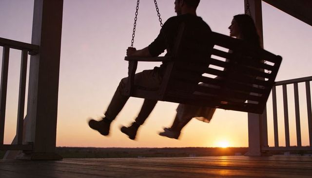 Silhouetted couple swinging on porch swing at golden sunset romantic veranda moment